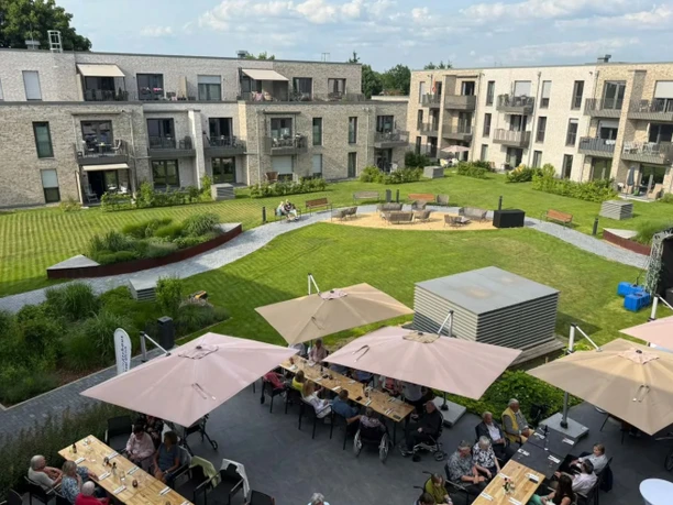 Blick vom Claras Restaurant auf den begrünten Innenhof des Schönes Leben Wolfsburg mit Sitzbereichen und angrenzenden Wohngebäuden.