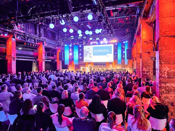 Managementkonferenz Halle Tor 2 Großer Konferenzsaal in Industriehalle mit Publikum vor beleuchteter Bühne und Präsentation