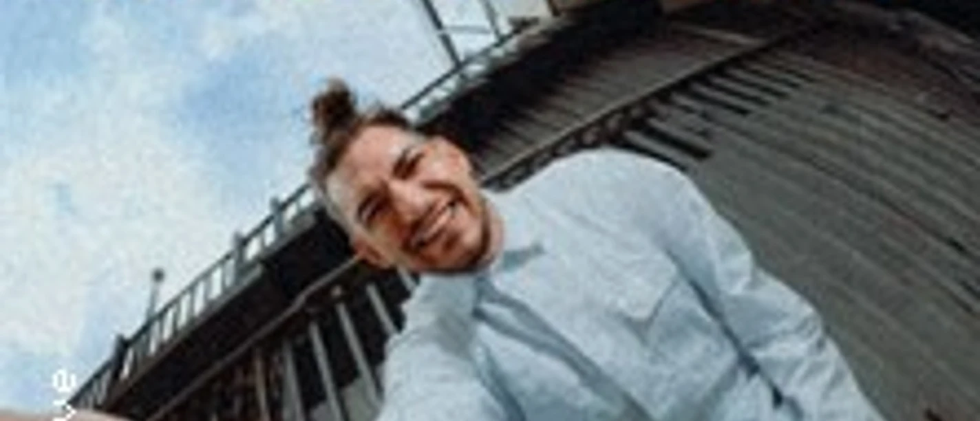 Lachende Person in weißem Outfit in Fisheye-Perspektive vor urbaner Kulisse mit rotem Tourtitel