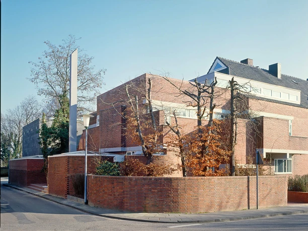 O.M. Ungers, Haus Belvederstraße, Köln 1990 Backsteinbau mit klaren geometrischen Formen hinter einer Mauer und kahlen Bäumen an einer Straßenecke.