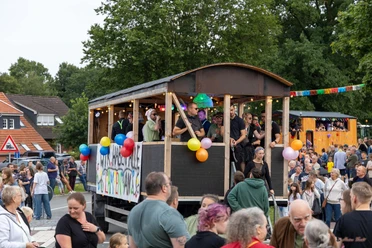 Festwagen.jpg Ein geschmückter Festwagen mit feiernden Menschen fährt bei einem Umzug an Zuschauern vorbei.