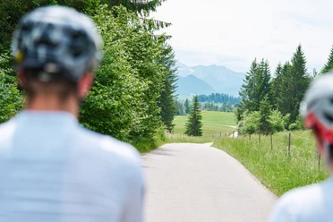 Bayerische Wallfahrt Zwei Radelnde vor einem Weg durch grünes Land und fernem Alpenpanorama