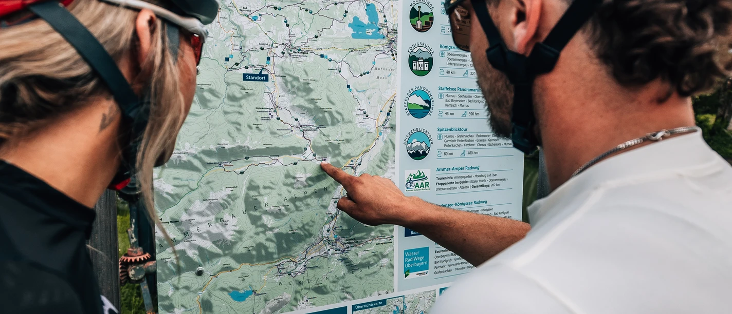Rund ums Ettaler Manndl Zwei Radelnde betrachten eine Übersichtskarte der Zugspitz Region.