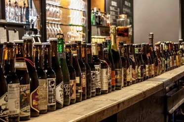 Theke, auf der viele verschiedene Bierflaschen aneinandergereiht stehen.