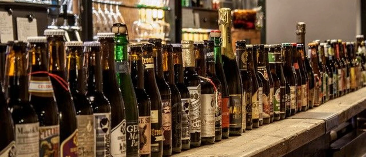 Theke, auf der viele verschiedene Bierflaschen aneinandergereiht stehen.