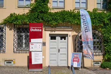 Eingang ins Museum Eingang zum Heimatmuseum Dohna mit Informationsschild und Fahne. Grüne Ranken an der Fassade.
