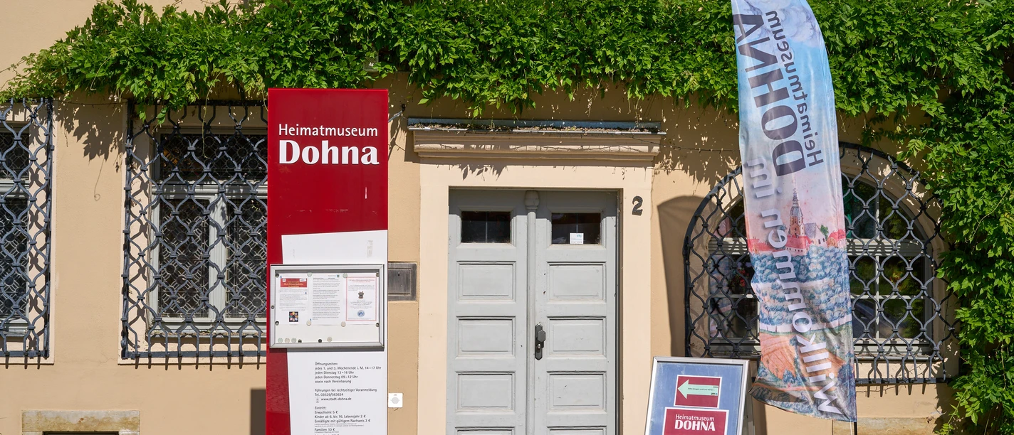 Eingang ins Museum Eingang zum Heimatmuseum Dohna mit Informationsschild und Fahne. Grüne Ranken an der Fassade.