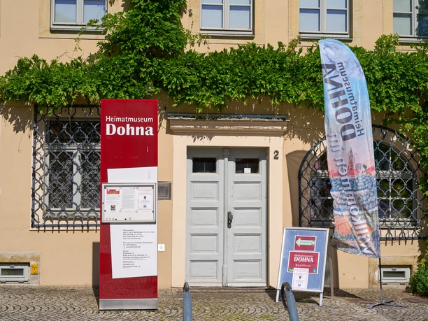 Eingang ins Museum Eingang zum Heimatmuseum Dohna mit Informationsschild und Fahne. Grüne Ranken an der Fassade.