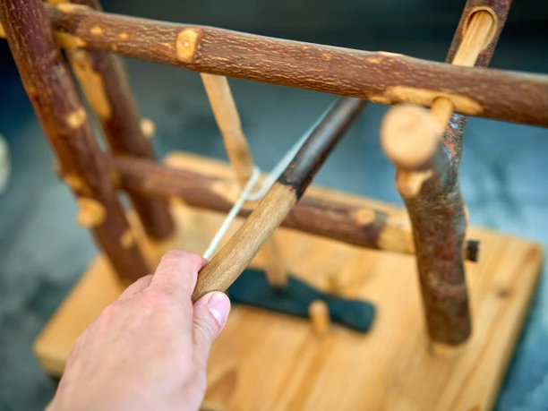 Holzgestell mit mehreren Ästen, eine Hand hält einen Ast, der auf das Gestell zeigt.