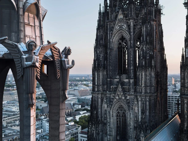 Koin 186 Blick auf gotische Türme und Figuren des Kölner Doms über der Stadt bei sanftem Abendlicht