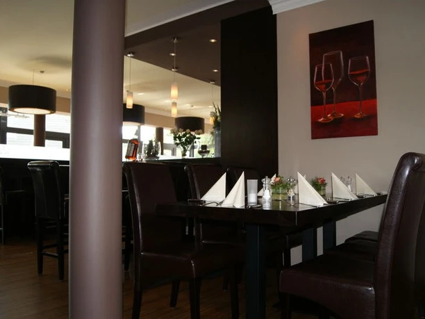 Rhodos Beschreibung: Gediegenes Restaurant mit dunklen Holzstühlen um lange Tische, Wandbild mit Weingläsern.