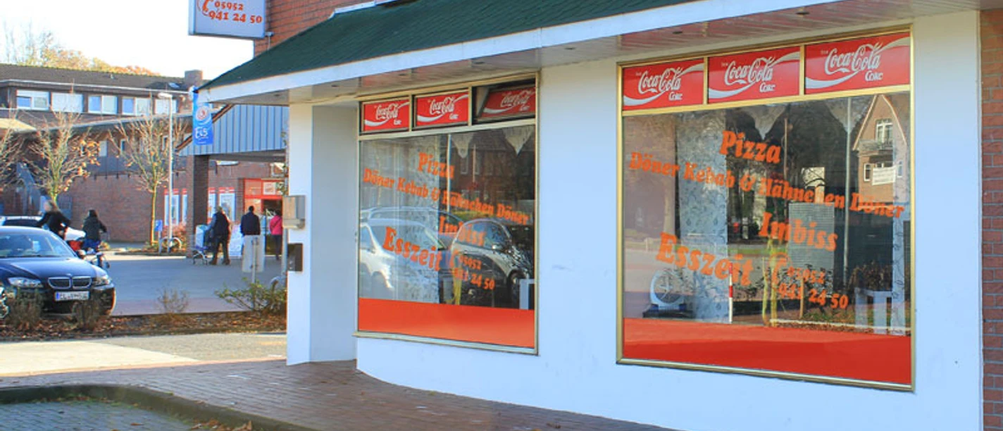 Esszeit Sögel Straßenansicht des Imbissrestaurants Esszeit in Sögel mit großer Fensterfront und Werbebeschriftung