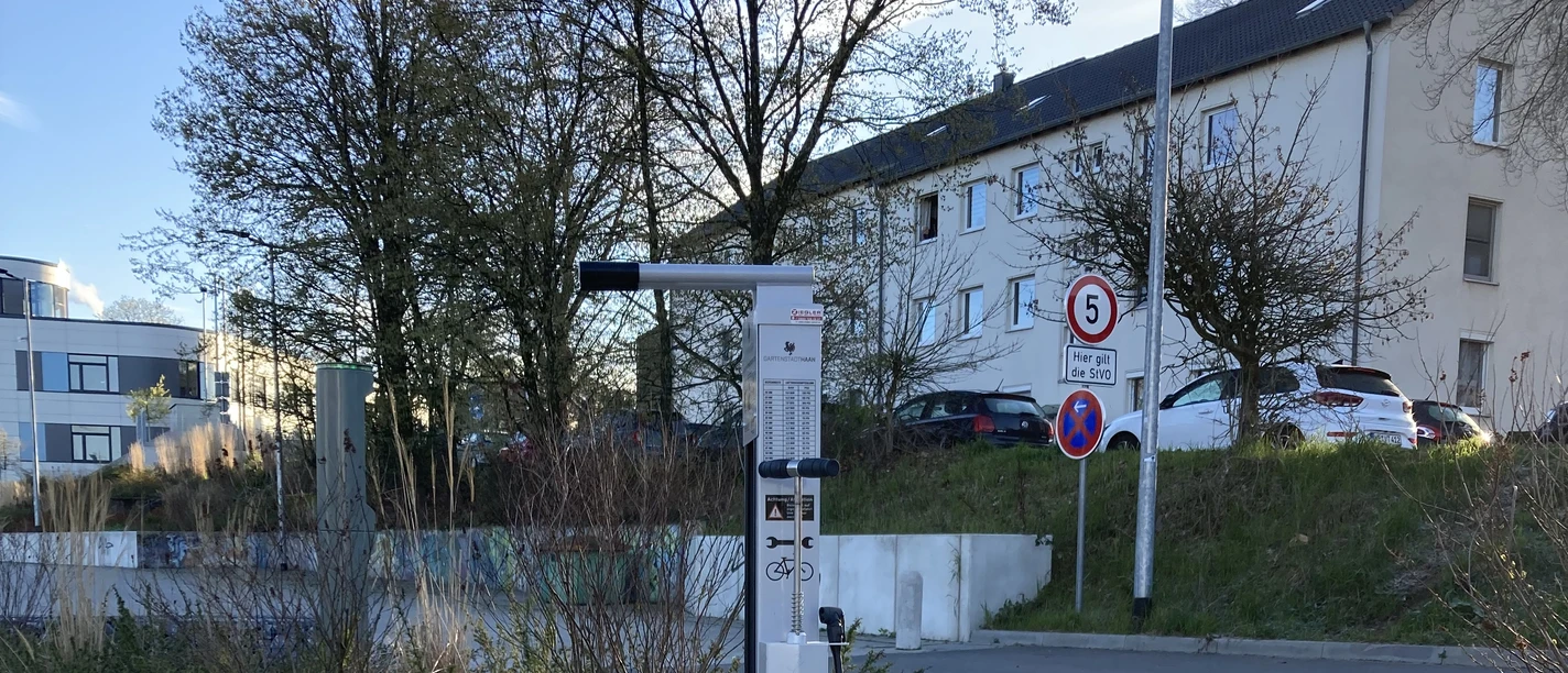 Fahrrad-Reparaturstation Parkplatz Sporthalle Adlerstraße Fahrrad-Reparaturstation mit Werkzeugen und Luftpumpe auf gepflastertem Untergrund.