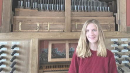 Musikalische Andacht mit Orgelmusik Junge Frau in rotem Pullover lächelt vor der großen, hölzernen Pfeifenorgel in der Pilsumer Kirche.