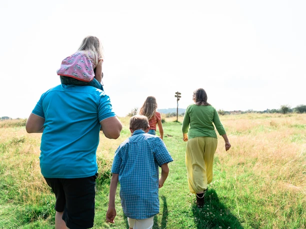 Dönche Eine Familie spaziert auf einer Wiese auf ein Wegweiserschild zu.