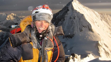 Bergsteigerin mit Helm und Sauerstoffmaske auf schneebedecktem Gipfel im Himalaya