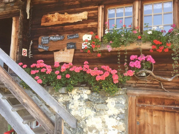 Façade en bois du restaurant de montagne, avec son escalier, ses géraniums et ses spécialités affichées