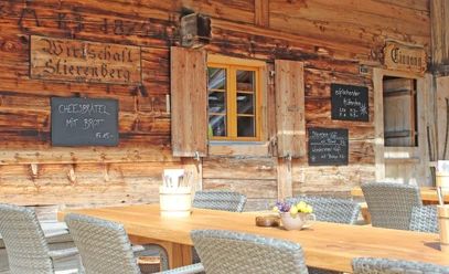 restaurant de montagne Stierenberg-terrasse avec soleil d'été Table en bois avec chaises grises devant le mur de l'auberge