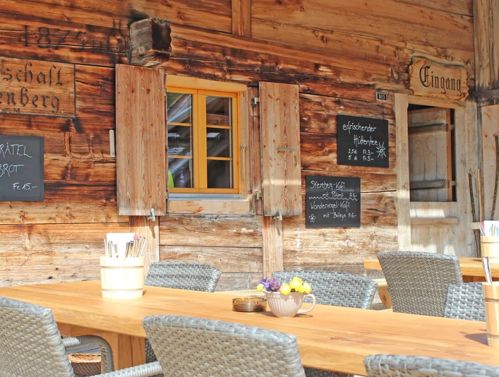 Stierenberg mountain restaurant terrace with summer sun Holztisch mit grauen Stühlen vor der Hauswand des GasthofsWooden table with gray chairs in front of the house wall of the innTable en bois avec chaises grises devant le mur de l'auberge