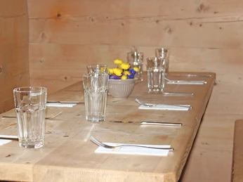 Gedeckter Tisch mit Bergblumendekoration Gedeckter Holztisch mit Bergblumen in einer HolzstubeWooden table set with mountain flowers in a wooden parlourTable en bois dressée avec des fleurs des montagnes dans une salle à manger en bois