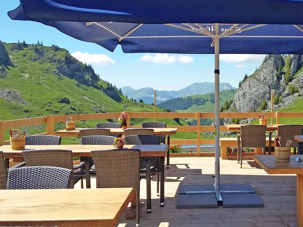 Vue de la terrasse en été à l'auberge de montagne Stierenberg Terrasse du restaurant d'altitude avec tables, chaises et parasols, entourée d'une clôture en bois