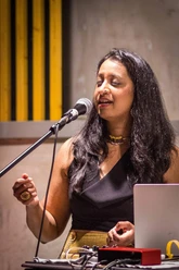 Musikerin am Dalit-Themenabend: Prashanthi Sankaran Musikerin singt am Mikrofon mit geschlossenen Augen vor Technikpult in warmem Bühnenlicht