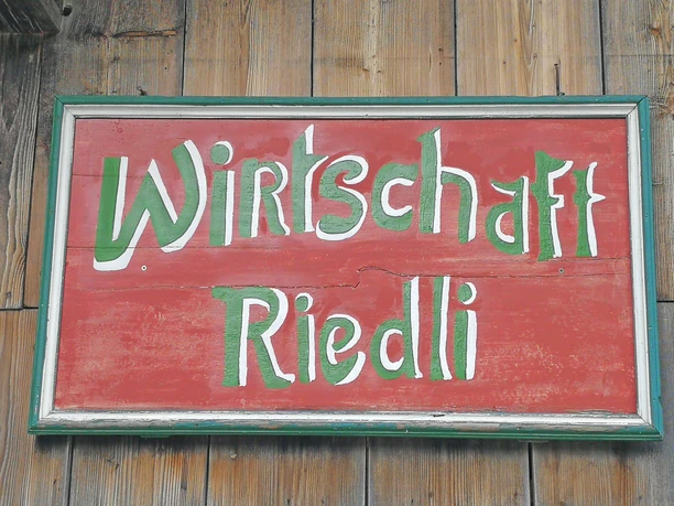 Shield of the restaurant Riedli Red wooden sign with the green and white inscription Riedli Wirtschaft