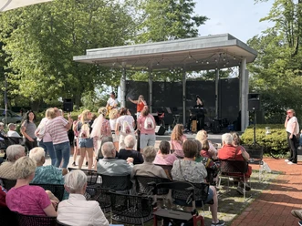 MusikamMeer.jpeg Dreiköpfige Band auf der Freilichtbühne im Kurpark Bad Zwischenahn. Im Vodergrund sitzen und tanzen viele Menschen