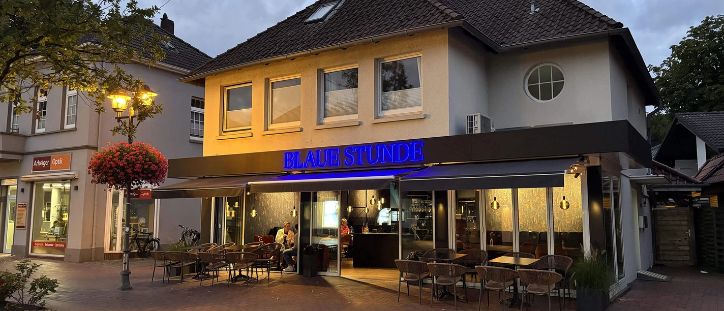 Blaue-Stunde-Bad-Zwischenahn-Aussenansicht.jpg Außenansicht der Bar Blaue Stunde in Bad Zwischenahn in der Abenddämmerung mit Außengastronomie.