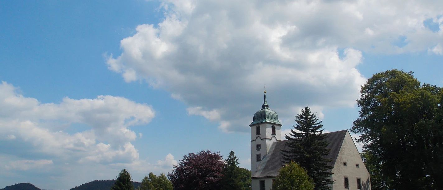 Kirche Papstdorf Man sieht eine Wiese und im Hintergrund die Kirche in Papstdorf