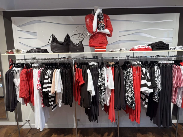 Mode-Spieker2.jpg Verkaufsraum von Mode Spieker. Kleiderstange und Regal mit Damenmode in Rot, Schwarz und Weiß.