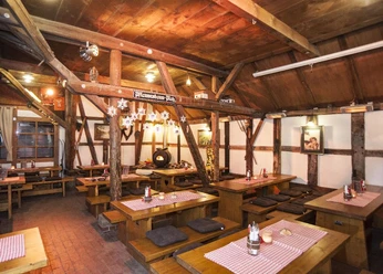 Hüttenparty Seekrug am Obernsee Innenansicht einer rustikalen Berghütte mit Holztischen, rot-weiß karierten Tischdecken und gedämpftem Licht.