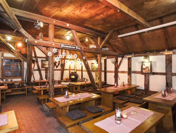 Hüttenparty Seekrug am Obernsee Innenansicht einer rustikalen Berghütte mit Holztischen, rot-weiß karierten Tischdecken und gedämpftem Licht.