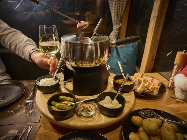 Lennestadt-Hohe_Bracht__Tourist-Information_Lennestadt&Kirchhundem_Klaus-Peter_Kappest_KPK1630744.jpg Ein Tisch mit Fondue, Beilagen und einer Hand mit Wein.