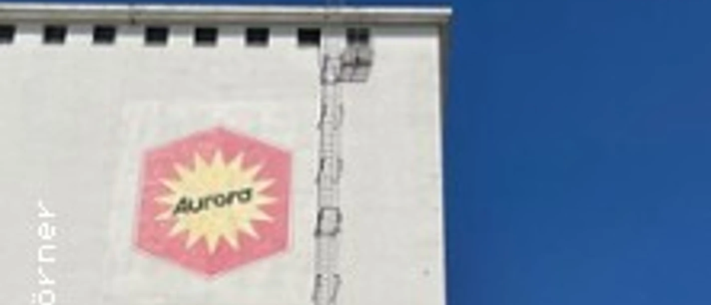 Weiße Hausfassade mit Aurora-Logo, Leiter und blauem Himmel am Deutzer Hafen