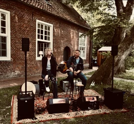HOPE Sängerin und Gitarrist des Duos HoPe spielen live im Freien vor einem alten Backsteingebäude.