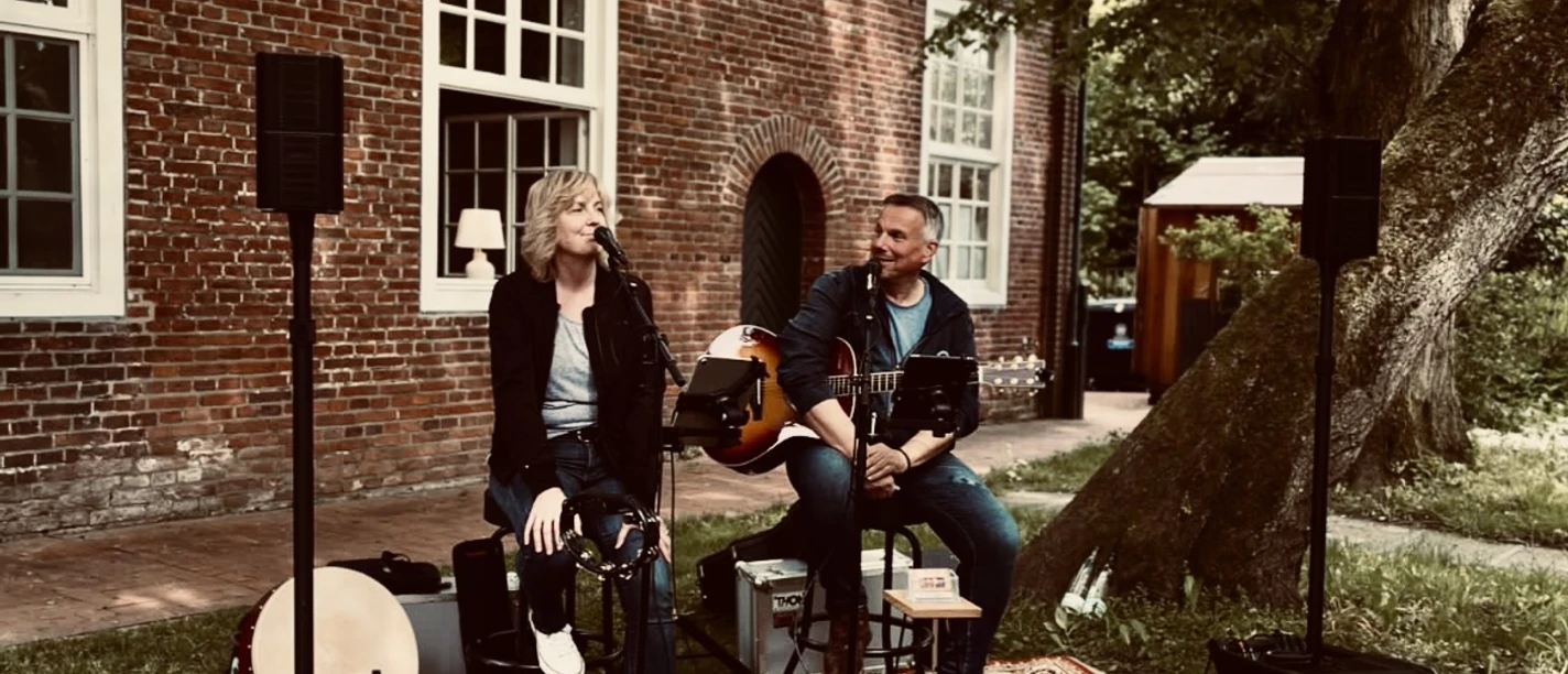 HOPE Sängerin und Gitarrist des Duos HoPe spielen live im Freien vor einem alten Backsteingebäude.