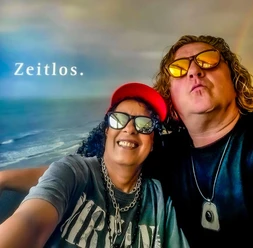 Gerrit Akkermann und Amina Die Musiker Gerrit und Amina als Selfie-Porträt vor einer Meereskulisse mit Schriftzug 'Zeitlos.'.