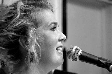 Jana Kremer Schwarz-Weiß-Porträt der Sängerin Jana Kremer bei einem Live-Auftritt am Mikrofon.
