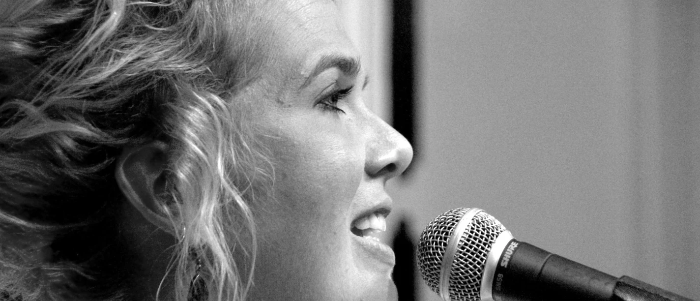 Jana Kremer Schwarz-Weiß-Porträt der Sängerin Jana Kremer bei einem Live-Auftritt am Mikrofon.