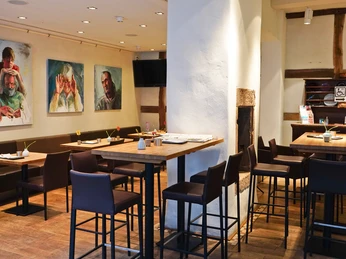 dsc00417 Ein stilvoll gestaltetes Café-Interieur mit hohen Tischen, dunklen Stühlen und moderner Kunst an den Wänden.