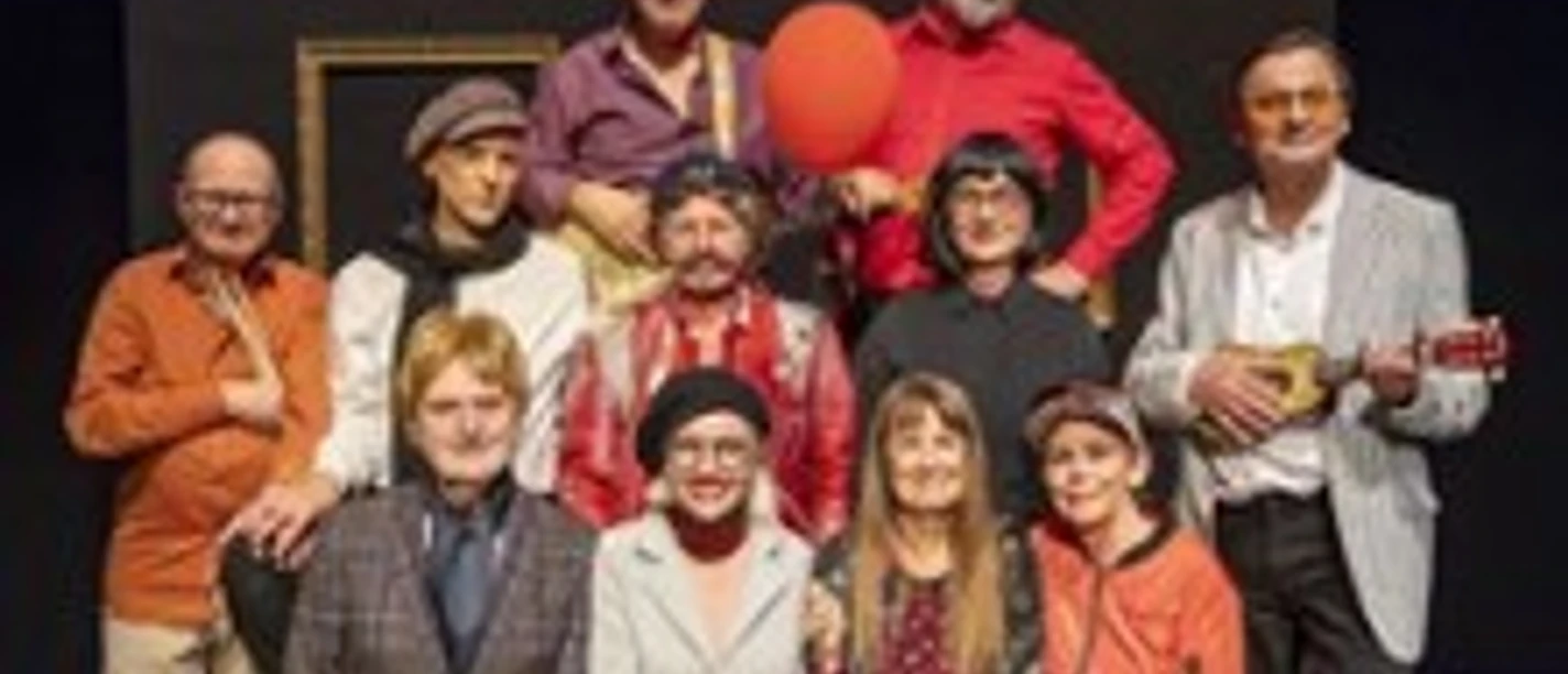Gruppenaufnahme von Bühnenkünstlern in farbiger Kleidung, einige mit Instrumenten.