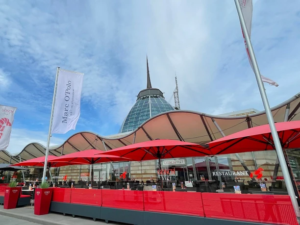 MOB_außenansicht_6_Bildrechte Mira Züchner Mehrwert_WEB.jpg Außenbereich eines Restaurants mit roten Sonnenschirmen vor dem modernen Shopping-Center Gebäude.