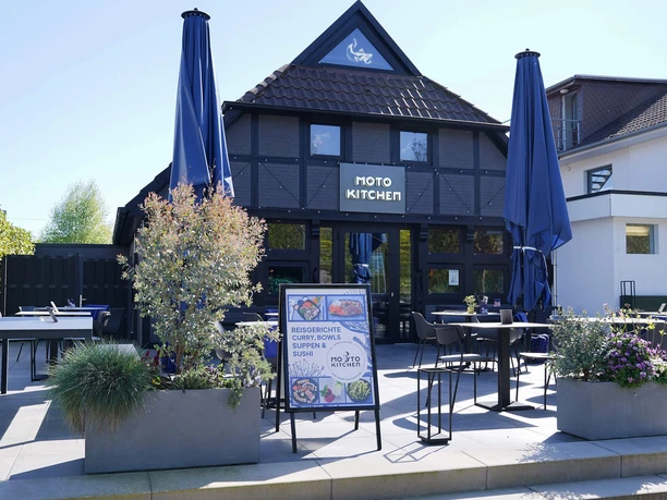 Moto-Kitchen-Bad-Zwischenahn-Aussenansicht.jpg Außenansicht des Restaurants Moto Kitchen in Bad Zwischenahn mit Terrasse und großen Sonnenschirmen.