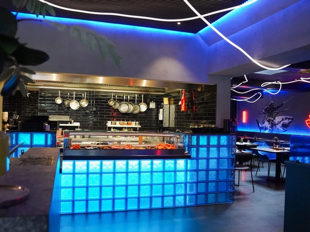 Moto-Kitchen-Bad-Zwischenahn-Thresen.jpg Der blau leuchtende Tresen aus Glasbausteinen und die offene Küche des modernen Restaurants.