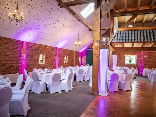 Meta-Goldener-Adler-Bad-Zwischenahn-Hochzeit2.jpg Festsaal für Hochzeiten mit Backsteinwänden, gedeckten Tischen und violetter Beleuchtung.