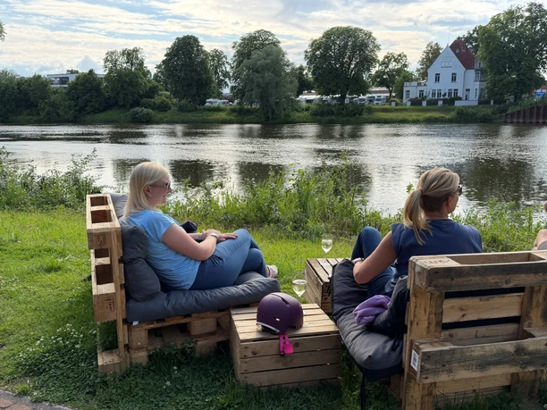 Weserstrand Beach Nienburg Zwei Frauen entspannen auf Palettenmöbeln bei einem Getränk mit direktem Blick auf die Weser.
