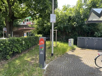 Fahrrad-Reparaturstation Richrather Straße / Schützenstraße Fahrrad-Reparaturstation am Wegesrand. Eine graue Säule mit Fahrradlogo nahe einer Brücke.