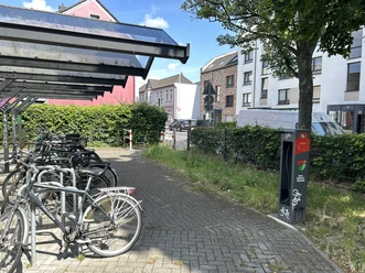 Fahrrad-Reparaturstation Richrather Straße / Schützenstraße Eine graue Fahrrad-Reparaturstation steht neben überdachten Fahrradständern mit mehreren Fahrrädern.