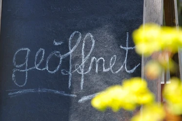 Betrieb geöffnet (Symbolbild) Tafel mit Kreideaufschrift "geöffnet" vor Zweigen